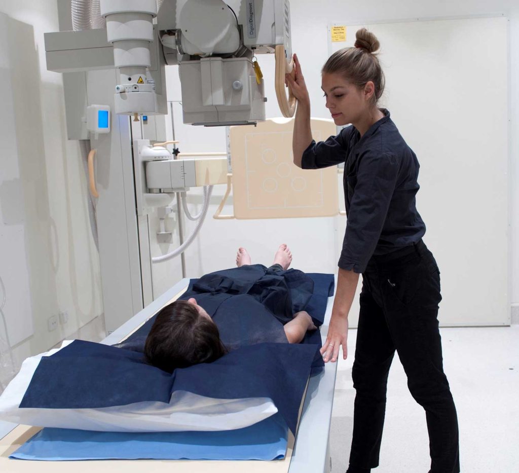 Radiographer positioning a patient for an X-ray examination in a diagnostic imaging room